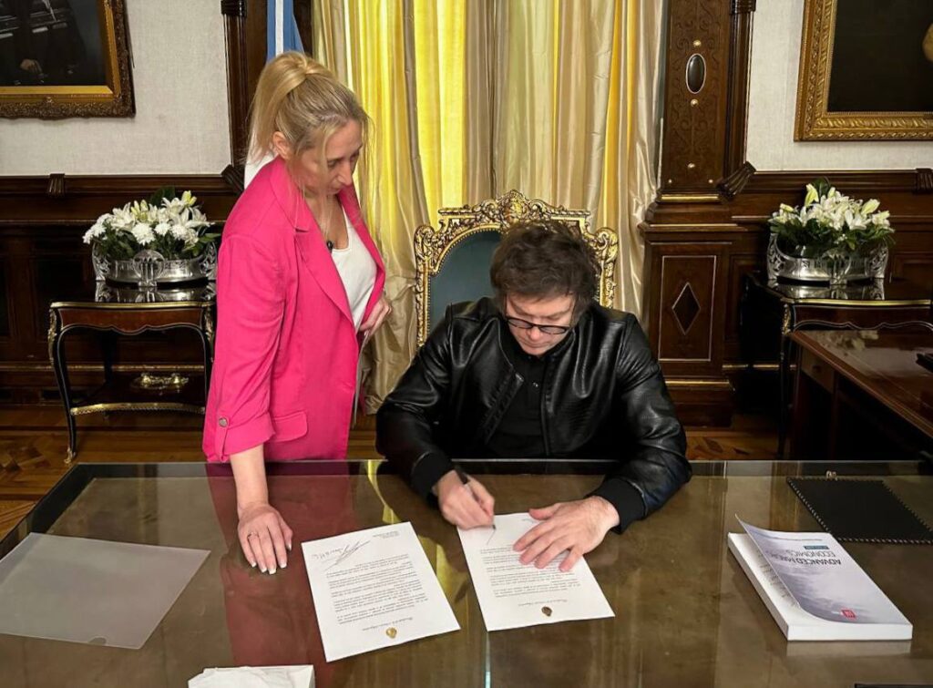 Milei firmando el texto en compañía de su hermana Karina, secretaria general de la Presidencia.